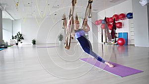 Athletic middle-aged woman doing aerial yoga in a hammock at the gym, in Standing Core Twist Pose Aerial.