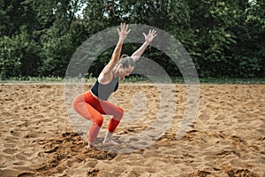 Athletic middle-aged woman doing fitness exercises on the sand of a sports ground