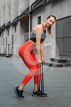Athletic middle-aged woman is engaged in fitness with an expander, on the street in the city