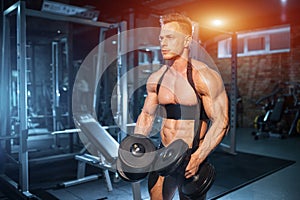 athletic muscular bodybuilder with torso has workout with dumbbell in gym