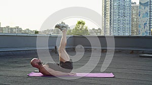 Athletic muscular guy doing active yoga on the roof of the house