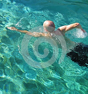 Athletic older adult male swimmer in sunlit blue water