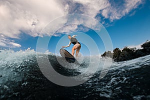 athletic one-armed man standing on surfboard and rides the wave. Wakesurfing on the river