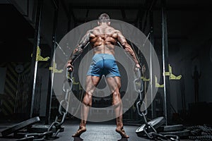 Athletic pumped man bodybuilder with chain in gym. Back view