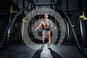 Athletic pumped man bodybuilder is engaged with ropes in hall of crossfit