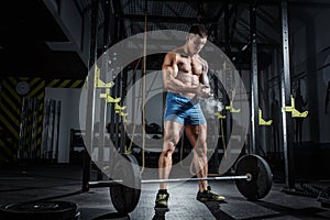 Athletic pumped man bodybuilder stands in front of bar in gym