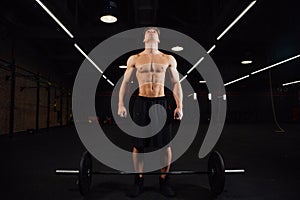 Athletic pumped man bodybuilder stands in front of bar in gym. Fitness male ready to work.