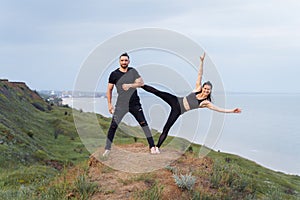 Athletic, pumped up, muscular, beautiful couple in love posing on the edge of the hill. Doing stretching and pair acro yoga on the