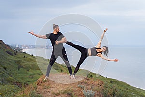 Athletic, pumped up, muscular, beautiful couple in love posing on the edge of the hill. Doing stretching and pair acro yoga on the