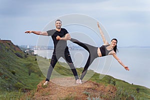 Athletic, pumped up, muscular, beautiful couple in love posing on the edge of the hill. Doing stretching and pair acro yoga on the