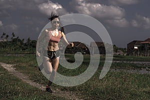 Athletic runner Asian woman training running series workout working hard outdoors on field background in harsh contrast light spor