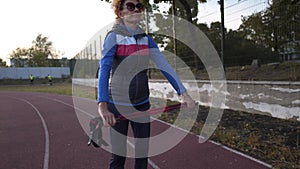 Athletic senior female doing physical exercise with stick on running track stadium before training Nordic walking