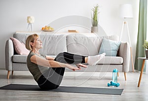Athletic senior woman doing abs exercises, sitting in boat yoga pose at home, free space