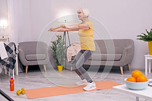 Athletic senior woman doing squats with health wand