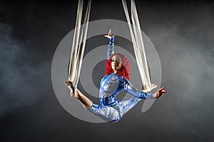 Athletic aerial circus artist with redhead in blue costume dancing in the air with balance