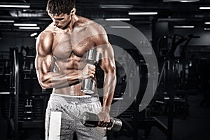 Athletic shirtless young sports man - fitness model holds the dumbbell in gym. Copy space fore your text.