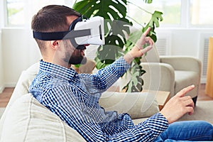 Athletic sir in virtual reality glasses sitting on sofa