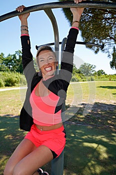 Athletic slim woman happy smiling sporting making pull-up exercises on a crossbar at outdoor street gym