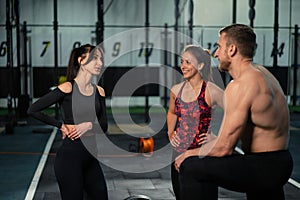 Athletic sport male athlete communicates with fit girls after training in hardcore gym. Fitness healthy man and woman tired after