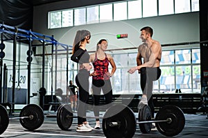 Athletic sport male athlete communicates with fit girls after training in hardcore gym. Fitness healthy man and woman tired after