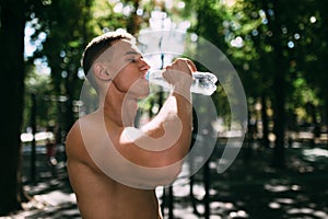 Athletic sport man drinking water from a bottle. Outdoor fitness.