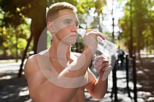 Athletic sport man drinking water from a bottle. Outdoor fitness.