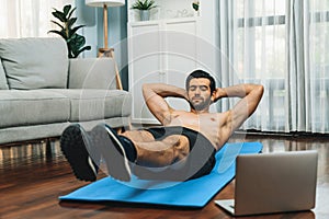 Athletic and sporty man doing crunch on fitness mat at gaiety home.