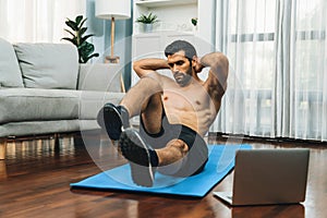 Athletic and sporty man doing crunch on fitness mat at gaiety home.