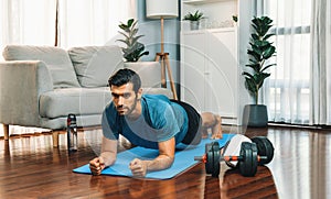 Athletic and sporty man doing plank on fitness mat at gaiety home.
