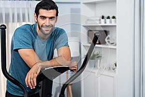 Athletic and sporty man running on elliptical running machine at gaiety home.