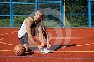 Athletic sporty man standing on basketball court ties his shoelaces before playing game.