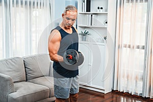 Athletic and sporty senior man lifting dumbbell at home. Clout