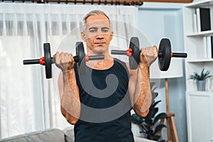 Athletic and sporty senior man lifting dumbbell at home. Clout