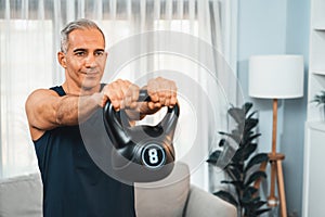 Athletic and sporty senior man lifting kettlebell at home. Clout