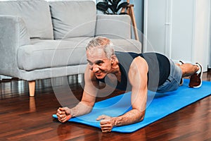 Athletic and sporty senior man planking on fitness exercising mat at home. Clout