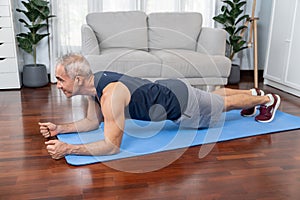 Athletic and sporty senior man planking on fitness exercising mat at home. Clout