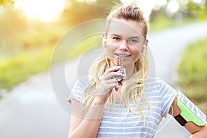 Athletic sporty woman eating protein bar after jogging in park