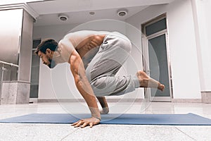 Athletic strong man practicing difficult yoga pose.