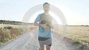 Athletic strong mature sportman resting and relaxing after running outside road through field.