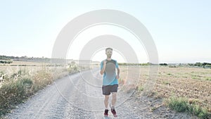 Athletic strong mature sportman running and looking at activity tracker on smart watch outside road through field.