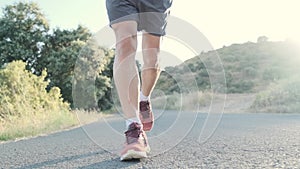 Athletic strong mature sportman wearing sport clothes while running outside road through field.