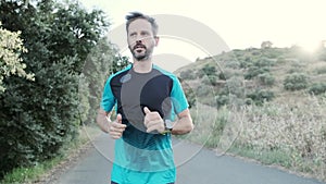 Athletic strong mature sportman wearing sport clothes while running outside road through field.