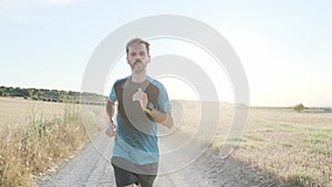 Athletic strong mature sportman wearing sport clothes while running outside road through field.