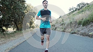 Athletic strong mature sportman wearing sport clothes while running outside road through field.