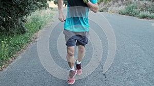 Athletic strong mature sportman wearing sport clothes while running outside road through field.