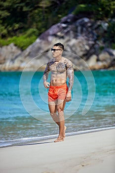 Athletic tattooed guy walking at the beach