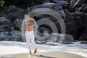 Athletic tattooed guy walking at the tropical beach