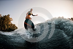 Athletic wet woman making trick with wakesurf on splashing wave.