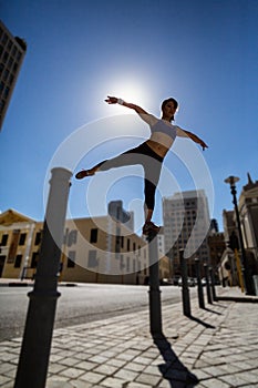 Athletic woman balancing on bollard and stretching out her arms and leg