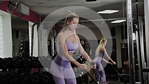 Athletic woman with a beautiful figure. Girl trains biceps on the simulator in the gym.